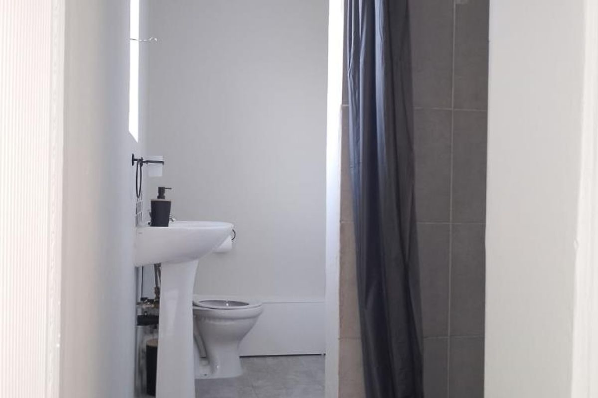 A functional bathroom featuring a pedestal basin, toilet, and a shower enclosure with grey tiled flooring and wall finishes.
