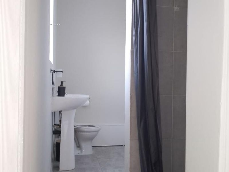 A functional bathroom featuring a pedestal basin, toilet, and a shower enclosure with grey tiled flooring and wall finishes.