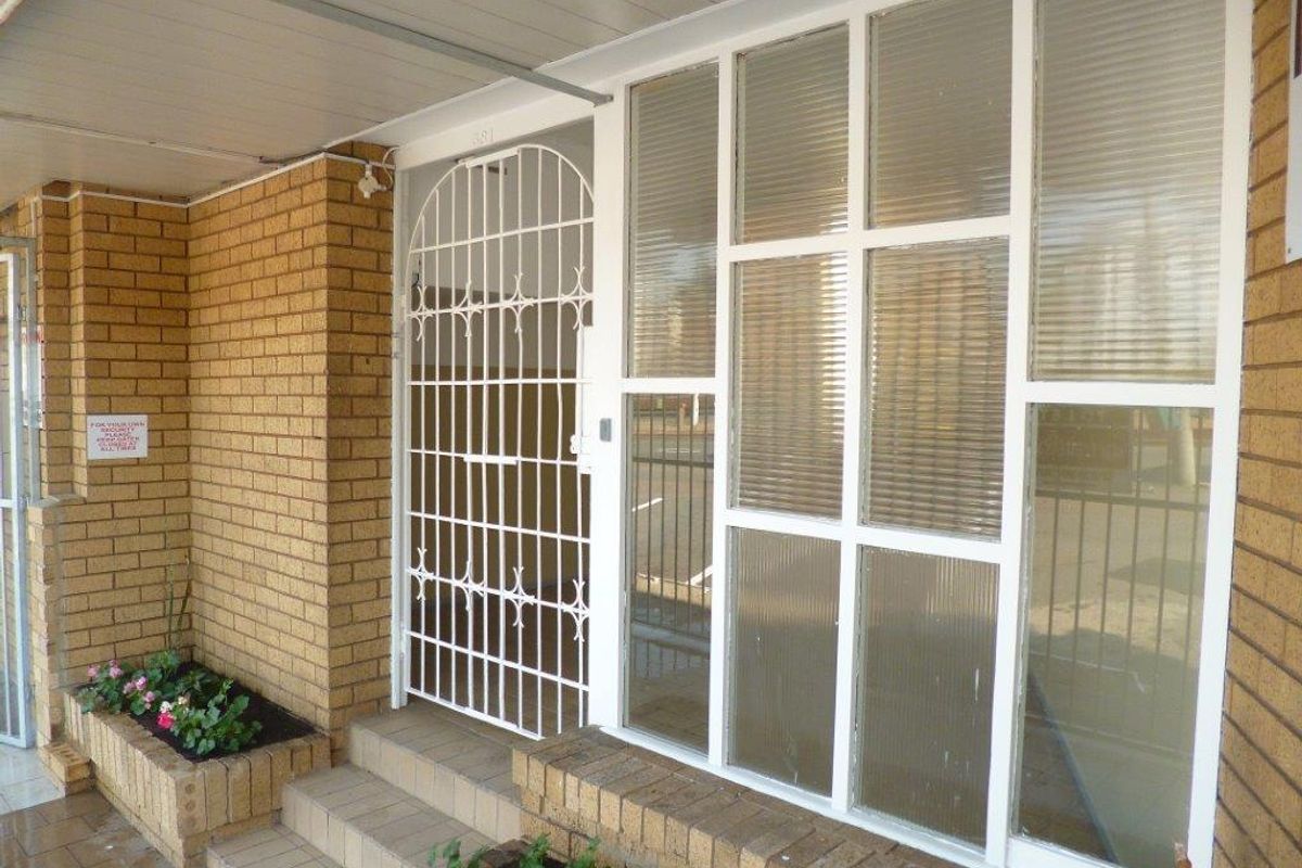 Entrance area featuring a brick facade, secure metal gate, and large multi-pane windows with a built-in planter box.