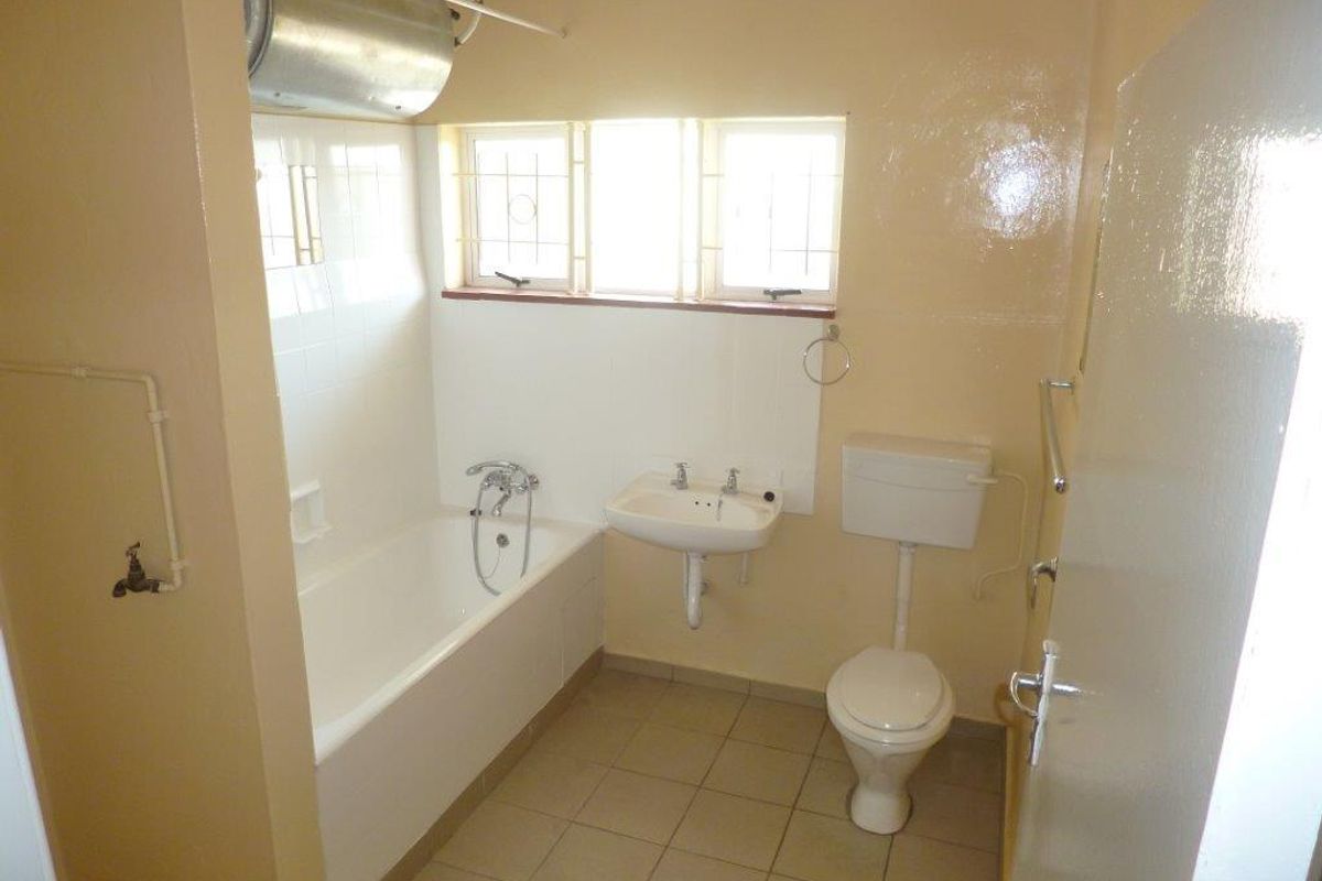 A functional bathroom featuring a bathtub, wall-mounted basin, and toilet, with tiled flooring and dated finishes, offering potential for modernization.