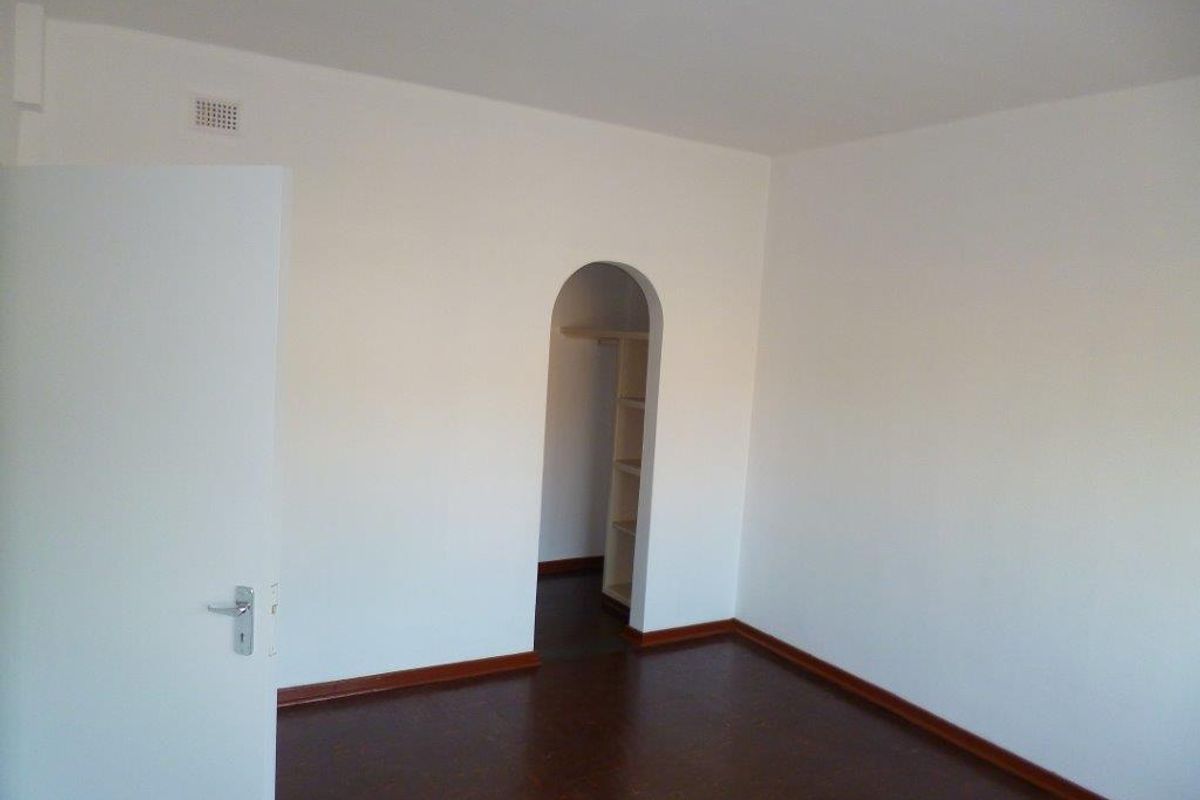 An empty bedroom featuring dark timber flooring, white walls, and a distinctive arched doorway leading to a built-in storage or closet area.