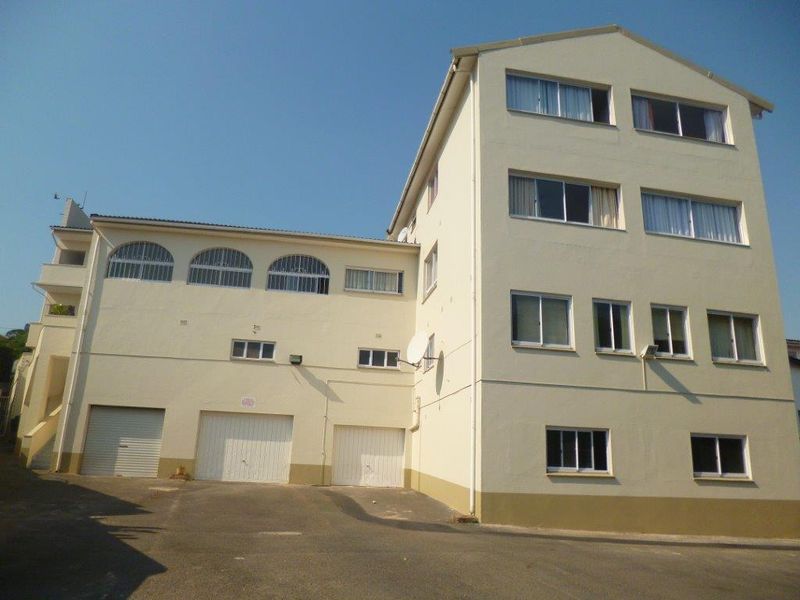 Exterior view of a multi-story apartment building featuring multiple garage doors, asphalt driveway, and various window styles including arched upper-level windows.