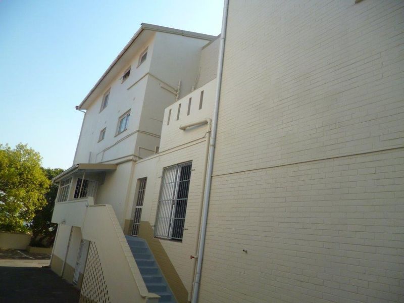 Rear exterior view of the apartment building featuring painted brick walls, an external staircase, and security-fitted windows.