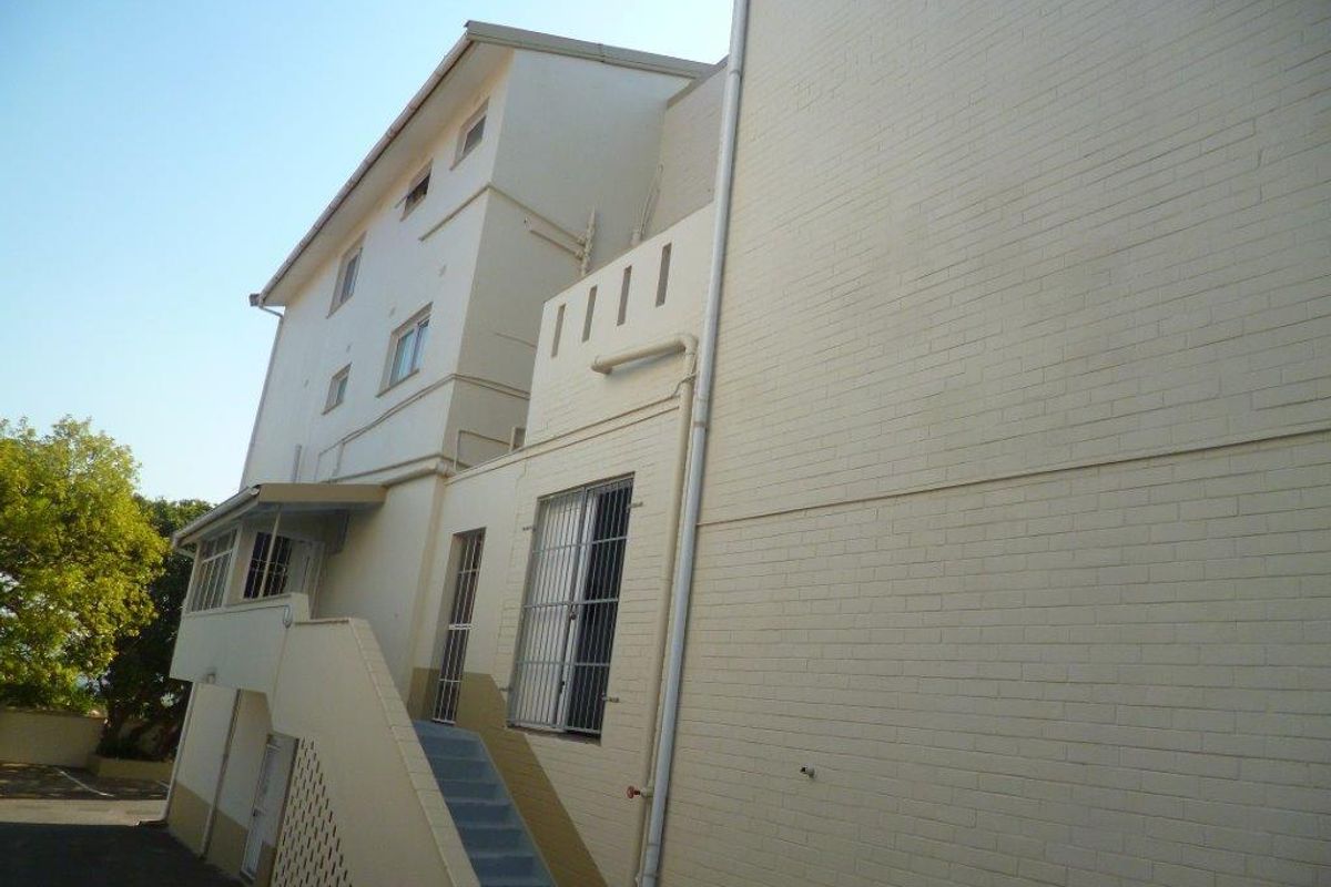 Rear exterior view of the apartment building featuring painted brick walls, an external staircase, and security-fitted windows.
