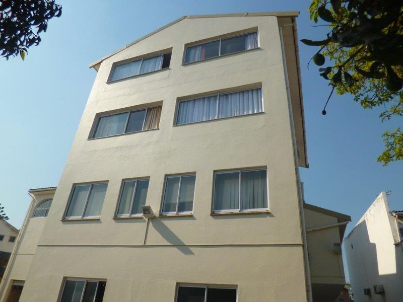 A low-angle view of the rear facade of a multi-story apartment building featuring multiple sliding windows and a neutral exterior finish.