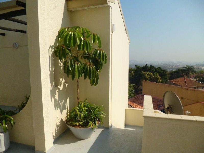 A private balcony area featuring a clean exterior finish, wall-mounted lighting, and elevated views over the surrounding neighborhood.