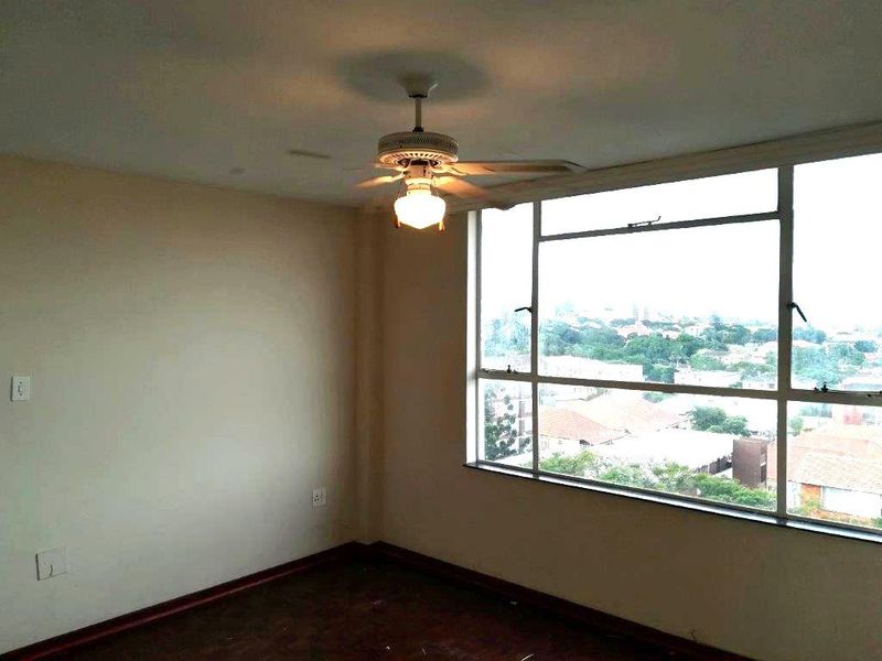 An empty bedroom featuring timber flooring, a ceiling fan, and a large window offering an elevated urban view.
