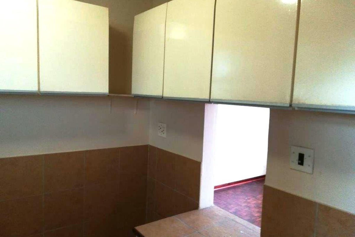 A compact kitchen area featuring built-in cabinetry, tiled backsplash, and a tiled countertop, currently in a dated condition.