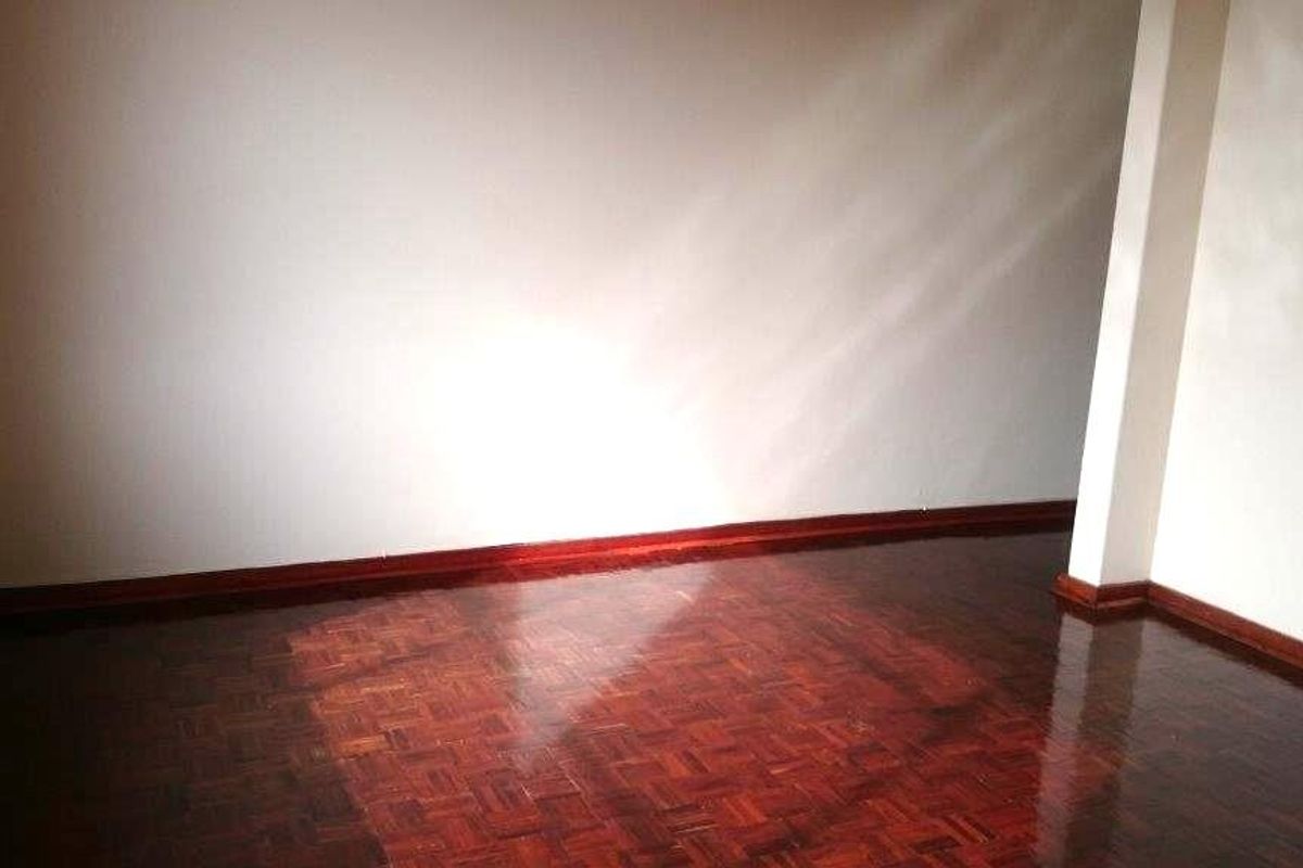 An empty living room featuring polished parquet flooring and neutral walls, offering a blank canvas for interior design.