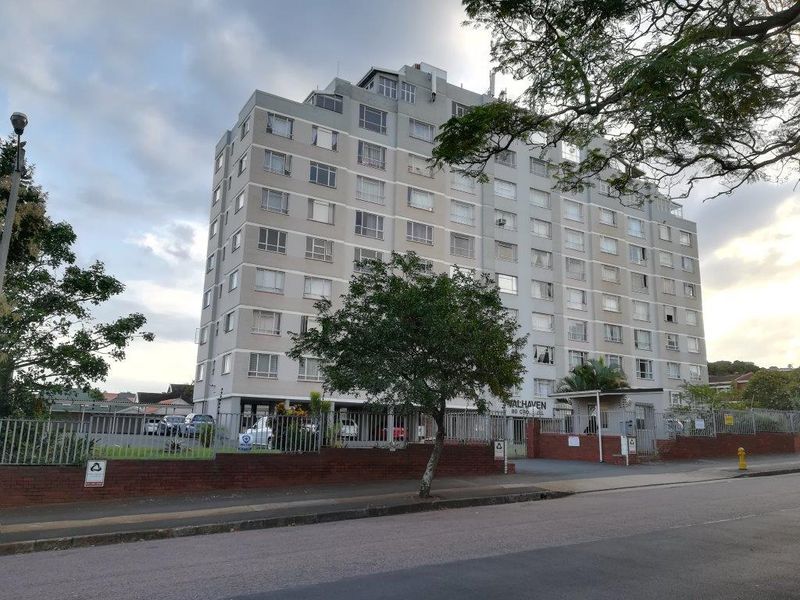 Exterior view of the multi-story Walhaven apartment building featuring a brick boundary wall, secure gated entrance, and paved driveway access.