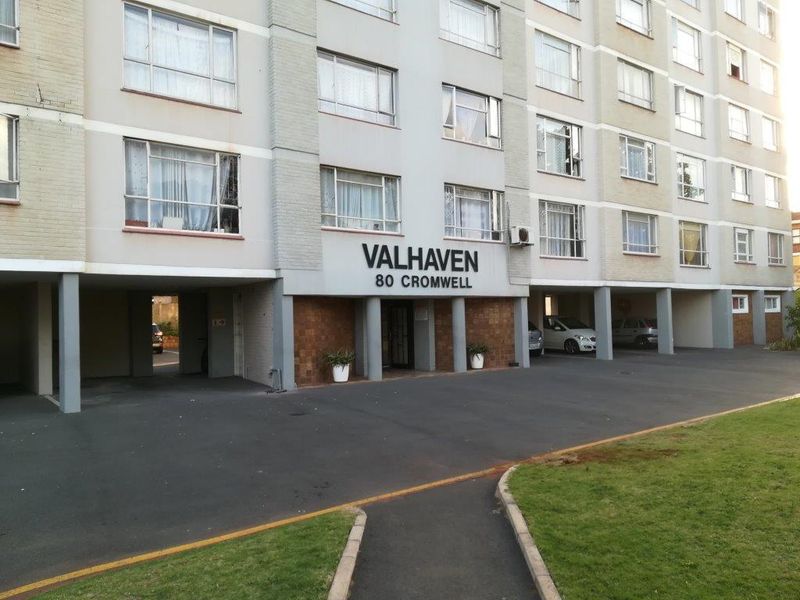 Front exterior view of Valhaven apartment building featuring a paved driveway, covered parking bays, and clear building signage.