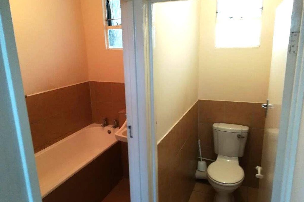 A functional bathroom featuring a bathtub and separate toilet area with neutral wall tiling and natural light from a window.