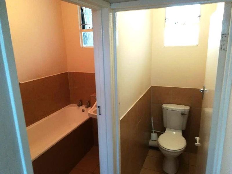 A functional bathroom featuring a bathtub and separate toilet area with neutral wall tiling and natural light from a window.