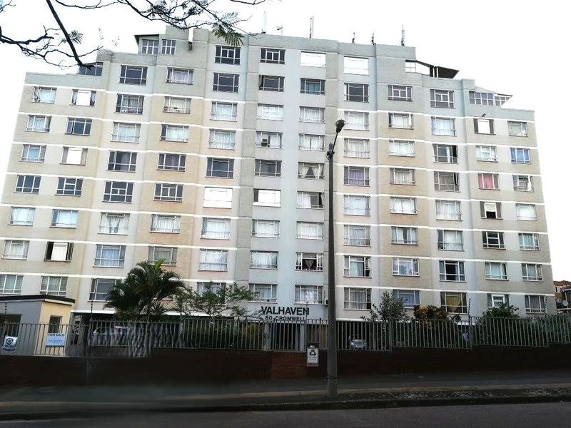 Front elevation view of Valhaven apartment complex, featuring a multi-story residential building with perimeter security fencing and street-level access.