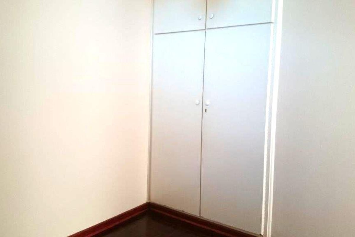 A simple, empty bedroom featuring dark timber flooring and a built-in wardrobe with overhead storage compartments.