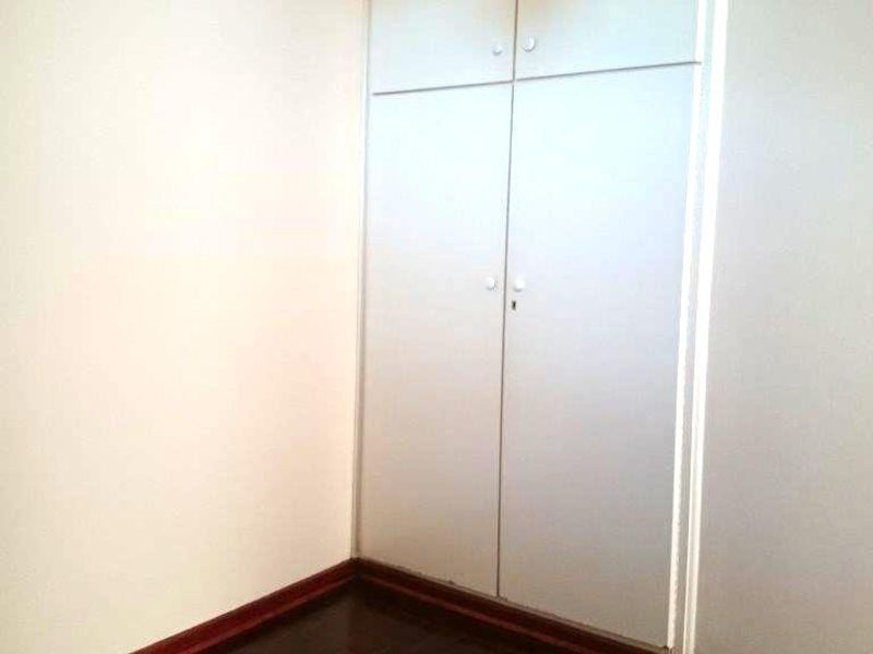 A simple, empty bedroom featuring dark timber flooring and a built-in wardrobe with overhead storage compartments.