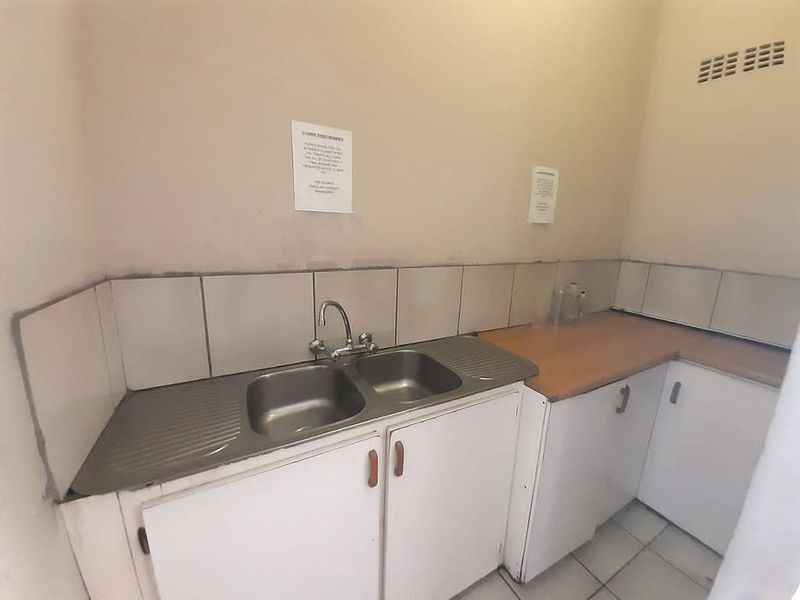 A functional scullery area featuring a double stainless steel sink, laminate countertops, and built-in base cabinetry with tiled splashbacks.