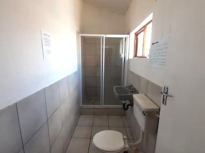 A functional bathroom featuring a shower enclosure, wall-mounted basin, and toilet with tiled finishes throughout.