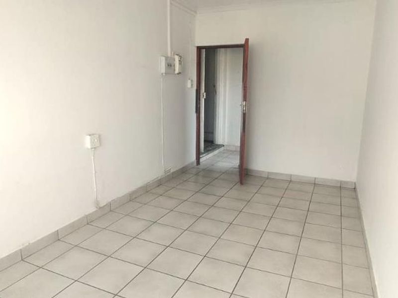 An empty, neutrally painted living area featuring tiled flooring and a standard doorway leading to an adjacent space.