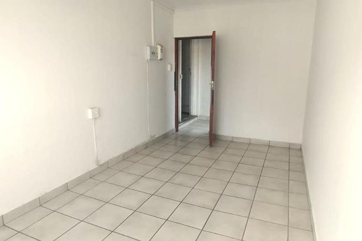 An empty, neutrally finished living area featuring tiled flooring and a doorway leading to an adjacent space.