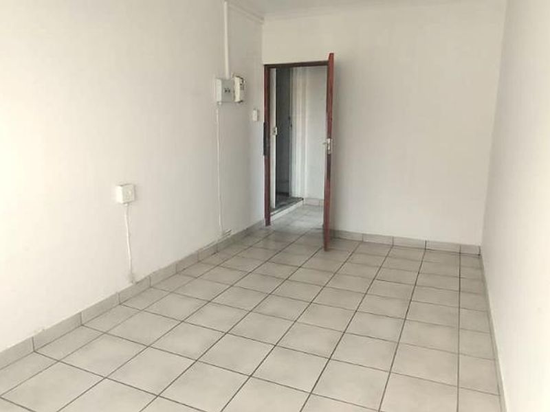 An empty, neutrally finished living area featuring tiled flooring and a doorway leading to an adjacent space.