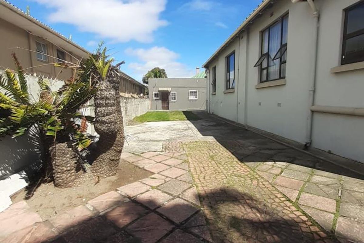 A rear exterior view of the property featuring a paved courtyard area, boundary walls, and side elevation of the building.