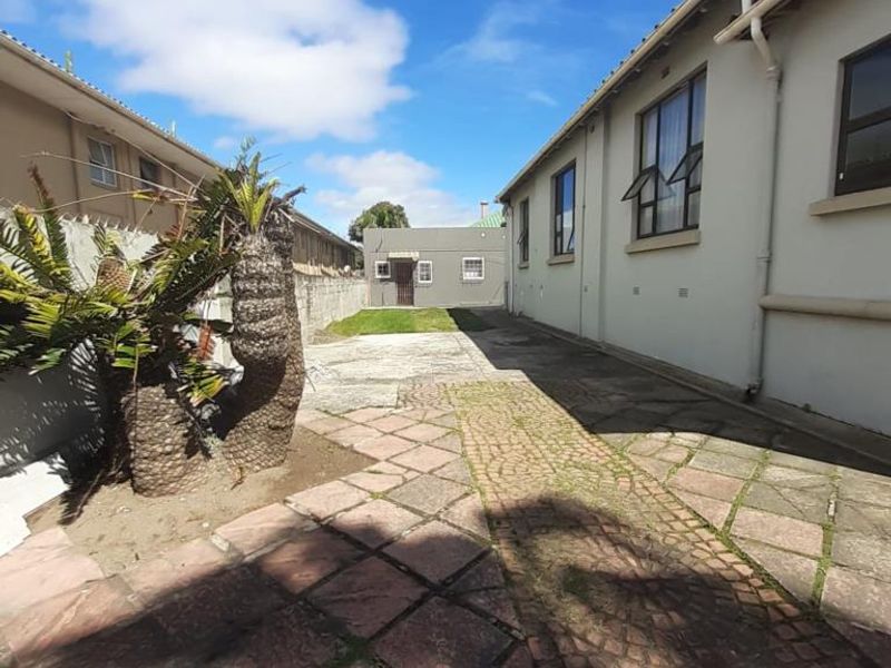 A rear exterior view of the property featuring a paved courtyard area, boundary walls, and side elevation of the building.