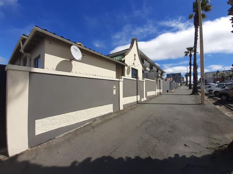 Street view of the apartment complex exterior, featuring a perimeter wall with security razor wire and a satellite dish installation.