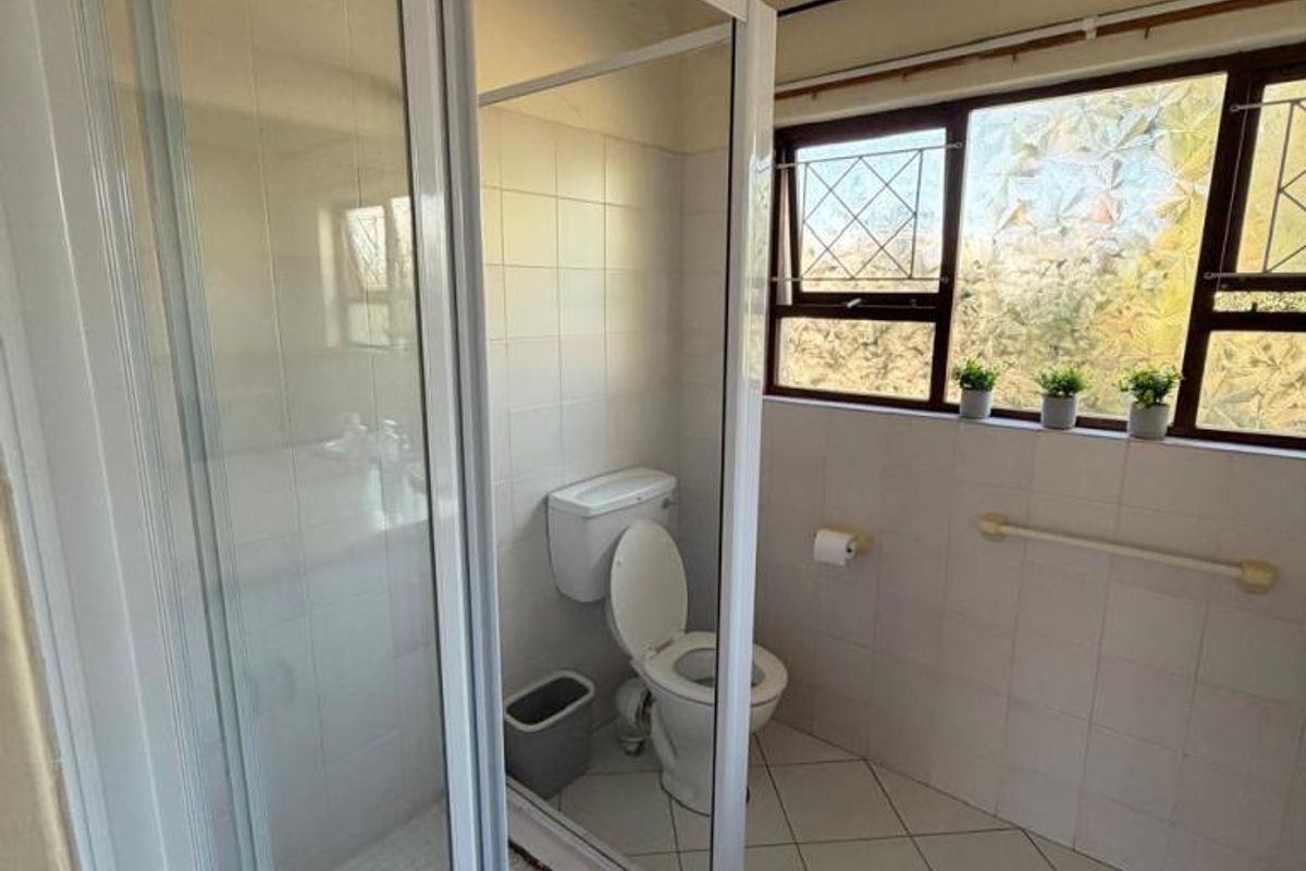 A functional bathroom featuring a glass shower enclosure, toilet, and tiled finishes, offering a clean space with potential for modern updates.
