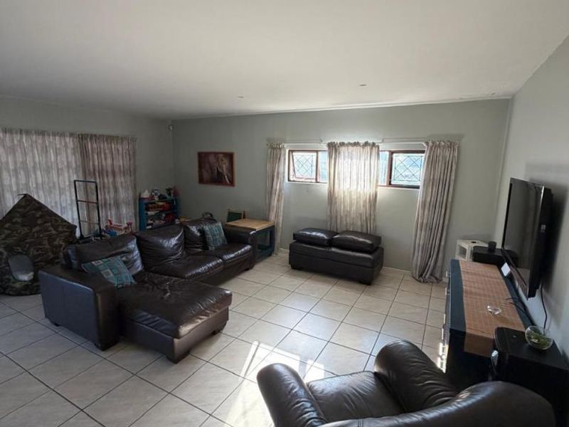 Spacious living room featuring neutral tiled flooring and multiple windows with leaded glass detailing, providing a bright and functional family living space.