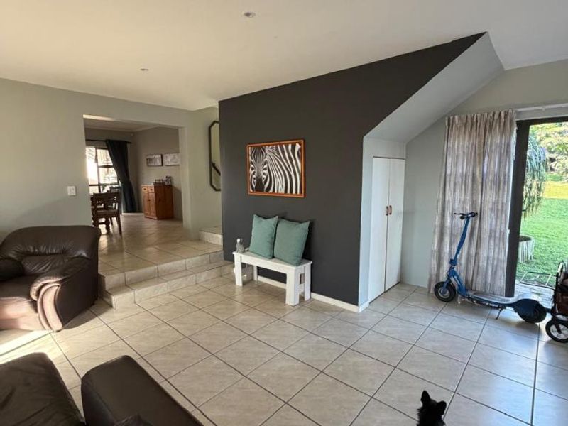 Spacious living area featuring tiled flooring, recessed lighting, and a built-in storage cupboard, with direct access to the garden through a sliding glass door.