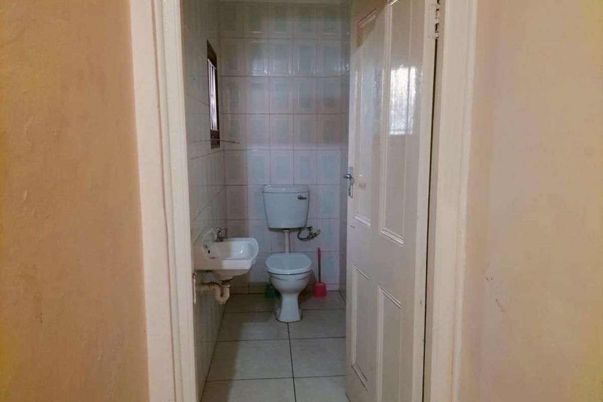A compact bathroom featuring a standard toilet, wall-mounted basin, and full-height wall tiling.