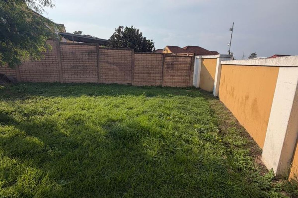 A private rear garden area featuring a grass lawn enclosed by brick and plastered boundary walls.