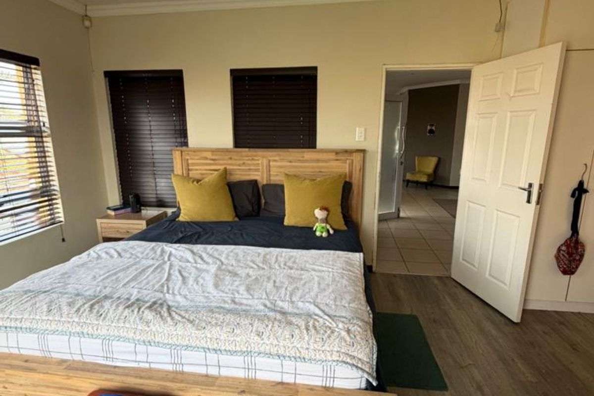 A spacious bedroom featuring wood-look laminate flooring, built-in cupboards, and recessed ceiling lighting, with an adjoining hallway view.