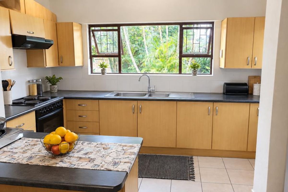 A functional kitchen featuring light wood cabinetry, dark laminate countertops, a double sink, and built-in cooking appliances with a view of the garden.