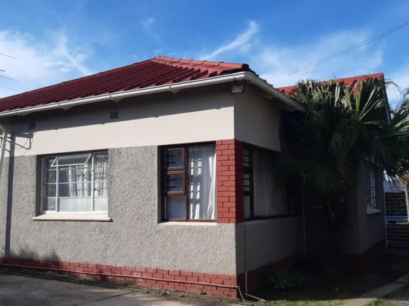 Front elevation of a single-story house featuring a tiled roof, textured plaster walls, and brick corner accents with metal-framed windows.