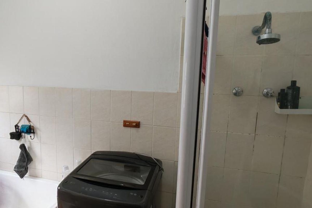 A functional bathroom featuring a shower enclosure, bathtub, and tiled wall finishes, showing signs of wear and dated fixtures.