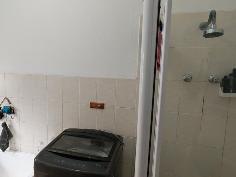 A functional bathroom featuring a shower enclosure, bathtub, and tiled wall finishes, showing signs of wear and dated fixtures.