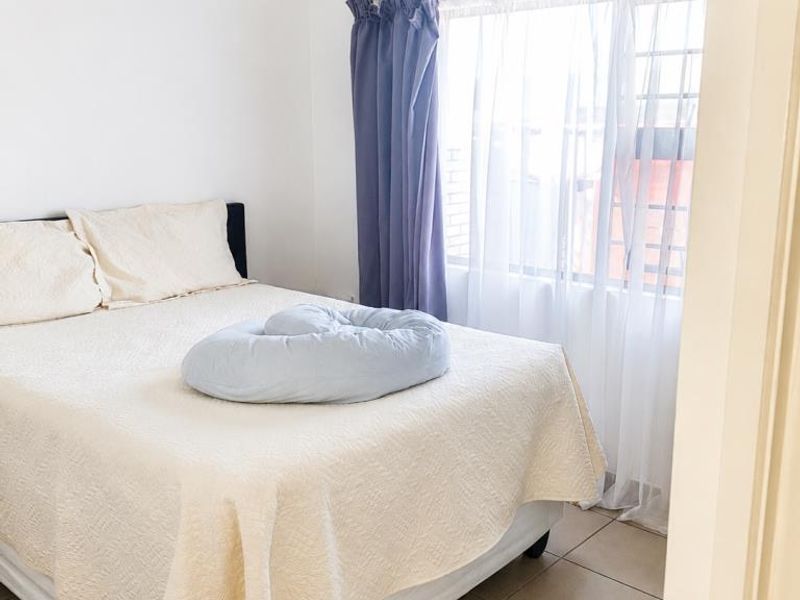 A bedroom featuring tiled flooring and a window fitted with security bars, offering a functional and neutral living space.