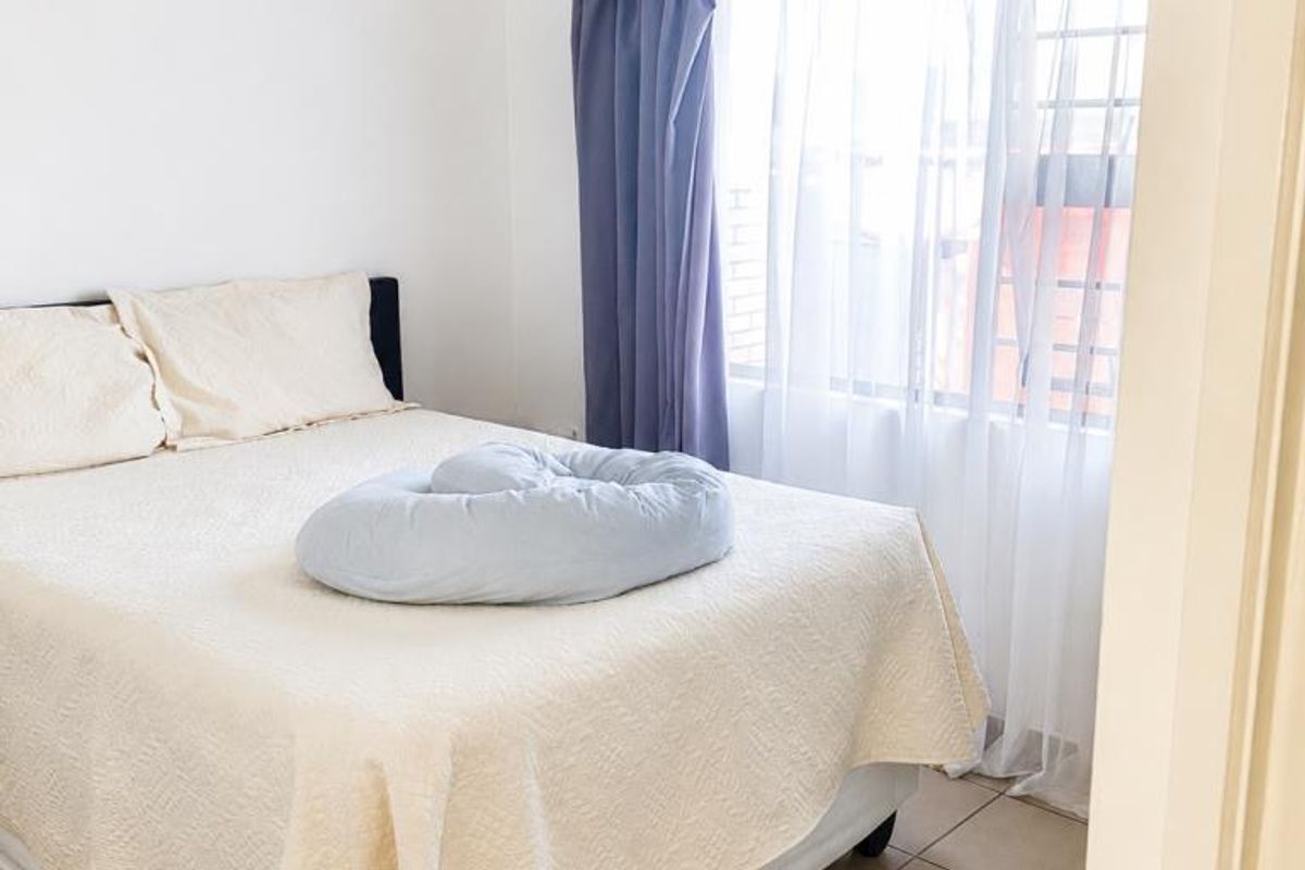 A bedroom featuring tiled flooring and a window fitted with security bars, offering a functional and neutral living space.