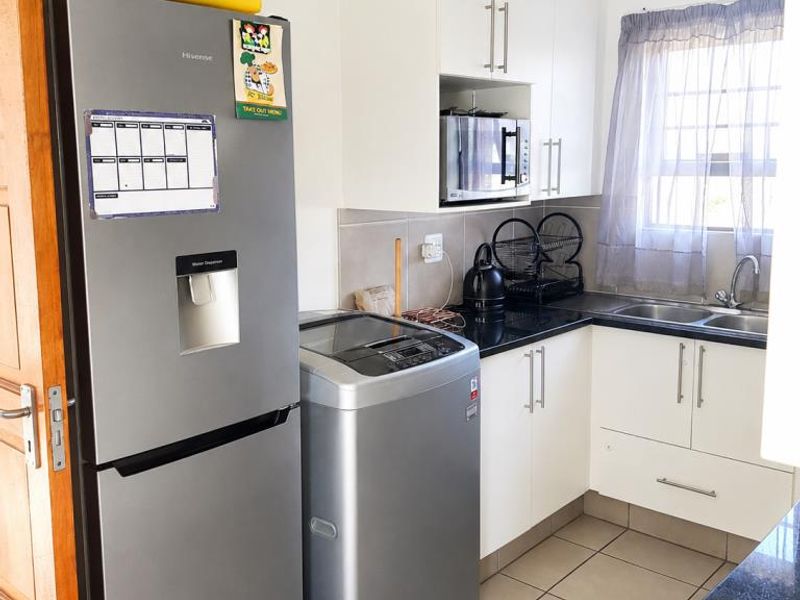 Compact kitchen featuring white cabinetry, granite countertops, double basin sink, and tiled flooring, providing a functional and efficient workspace.