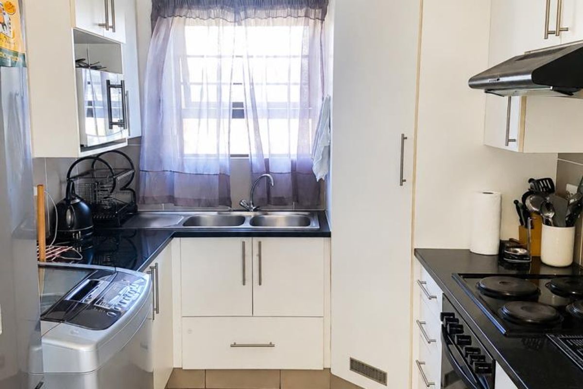 Compact kitchen featuring white cabinetry, black countertops, built-in oven, electric hob, extractor fan, and tiled flooring.