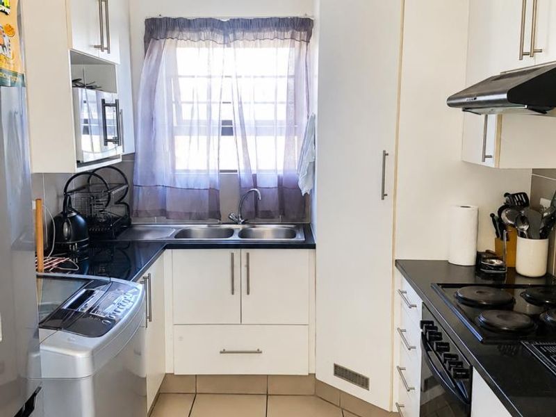 Compact kitchen featuring white cabinetry, black countertops, built-in oven, electric hob, extractor fan, and tiled flooring.
