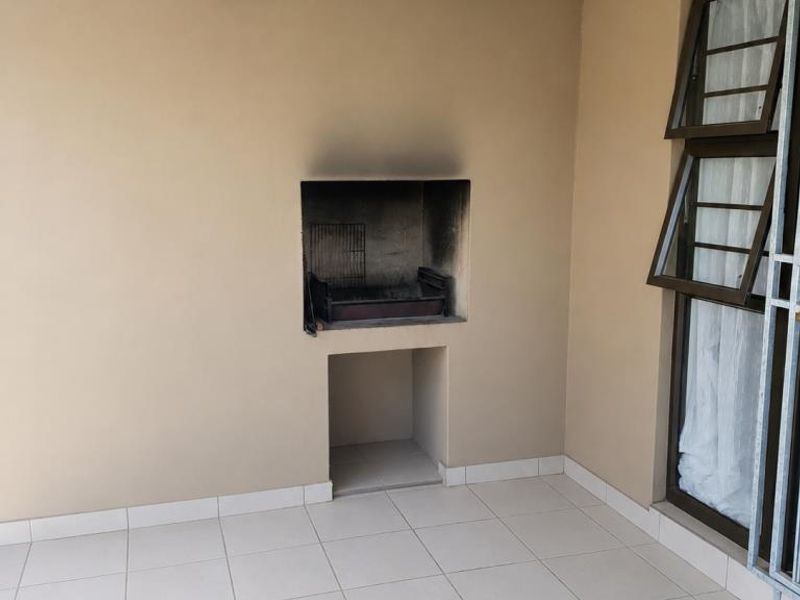 Covered patio area featuring tiled flooring and a built-in braai, providing a functional outdoor entertainment space.