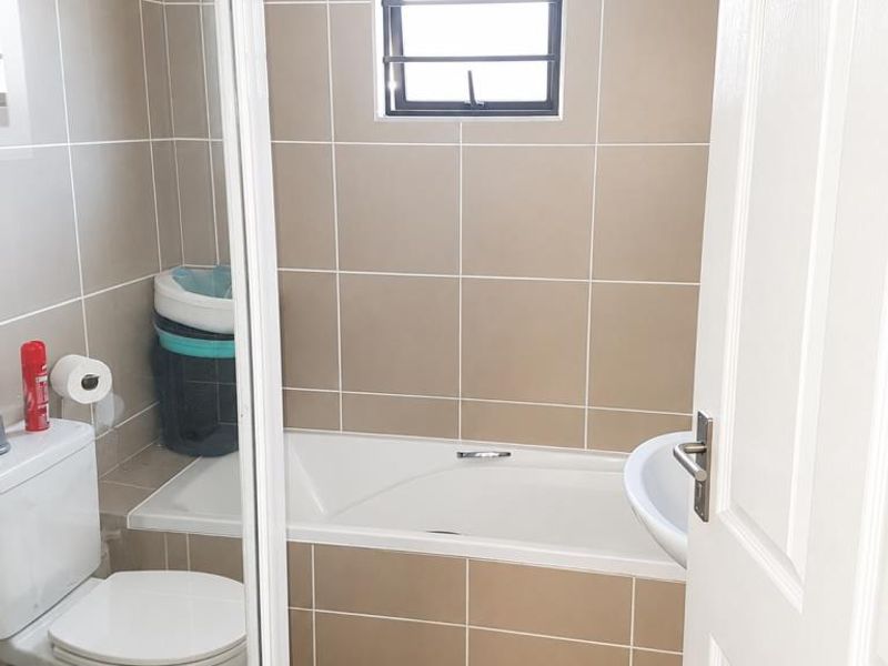 A functional bathroom featuring a built-in bathtub, pedestal basin, toilet, and a separate shower enclosure with neutral wall tiling.