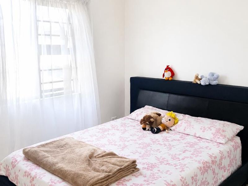 A simple bedroom featuring tiled flooring and a window fitted with security bars, providing a functional and neutral space.