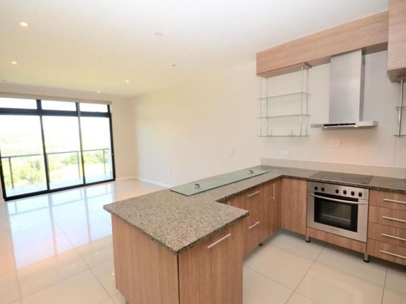 Modern open-plan kitchen and living area featuring granite countertops, built-in appliances, tiled flooring, and large sliding doors leading to a balcony.
