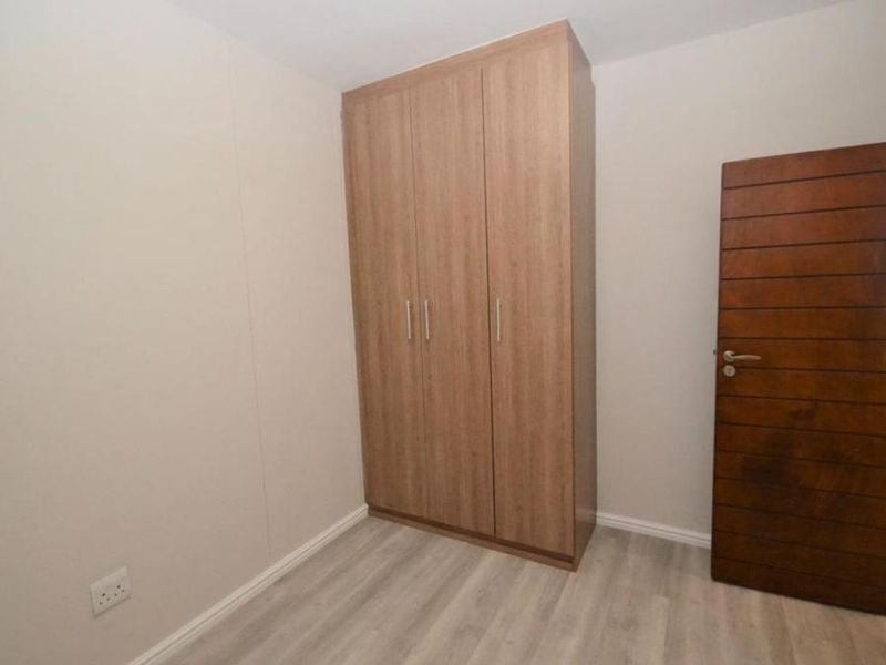 A clean, empty bedroom featuring light-toned laminate flooring, neutral walls, and a modern built-in wooden wardrobe.