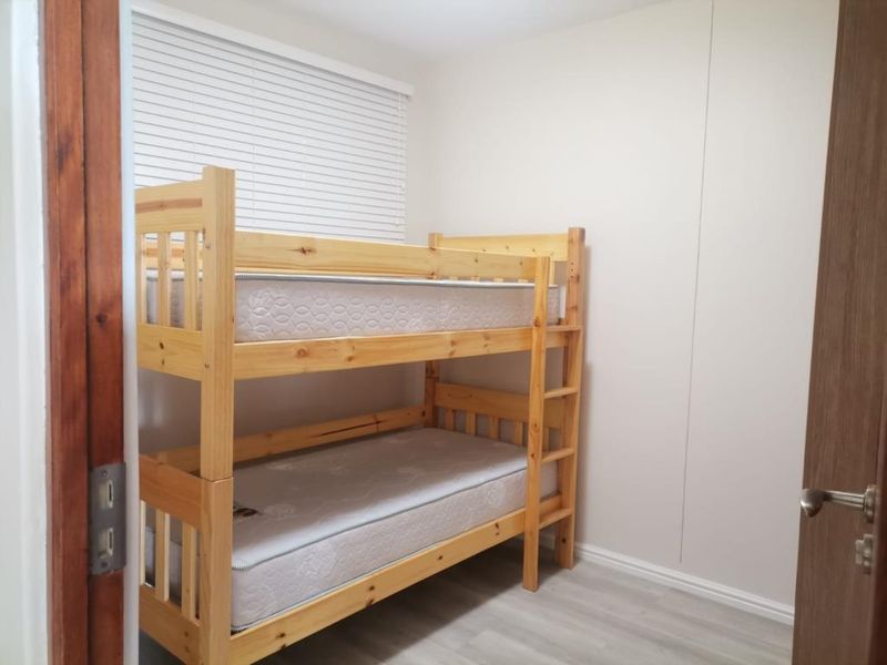A compact bedroom featuring light-toned laminate flooring, neutral walls, and fitted venetian blinds, providing a clean and functional space.