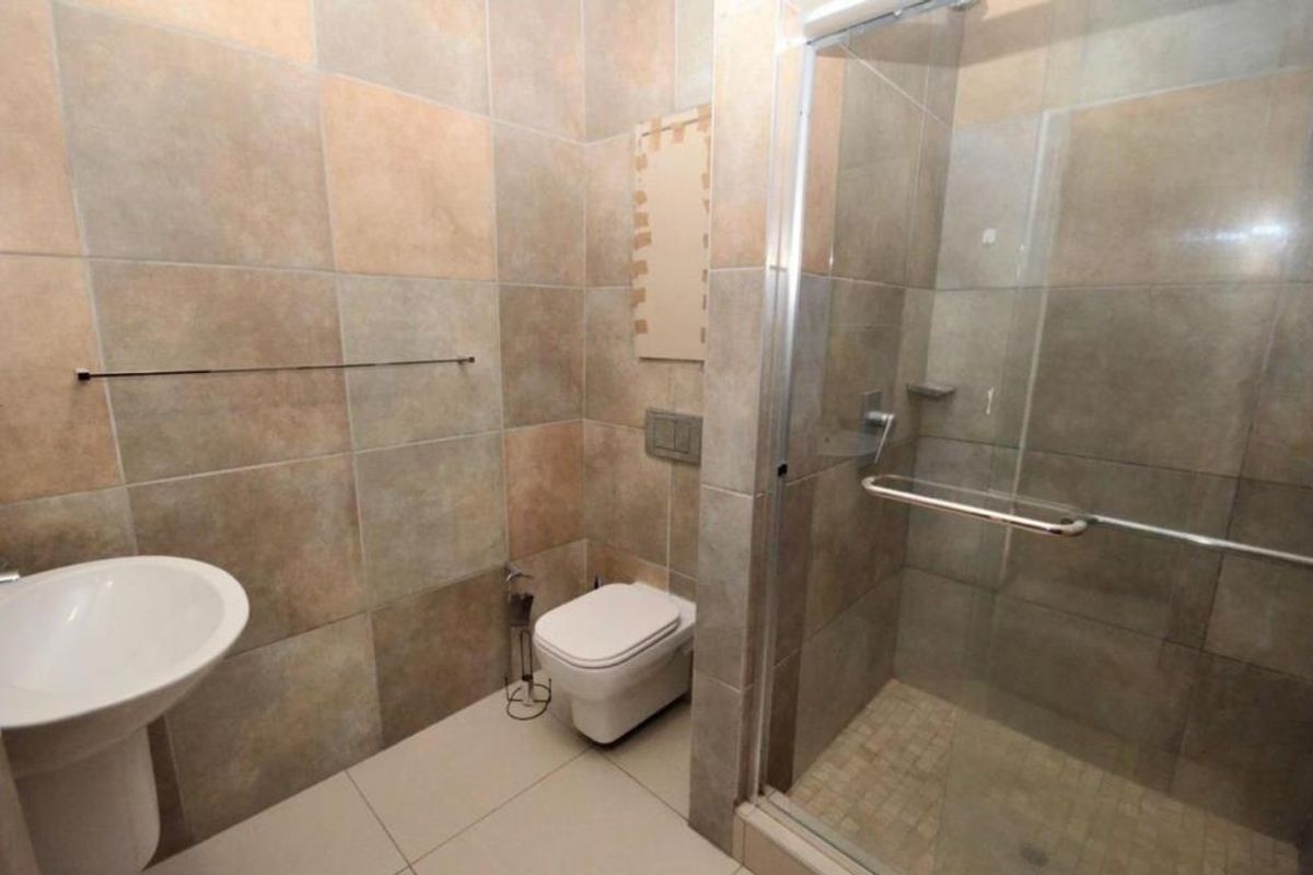 A modern bathroom featuring a pedestal basin, wall-hung toilet with concealed cistern, and a glass-enclosed shower with neutral wall and floor tiling.